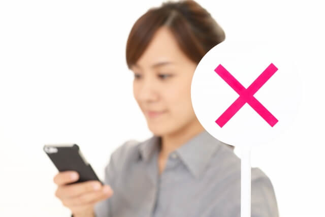 スマホをもち✖のプラカードを出す女性